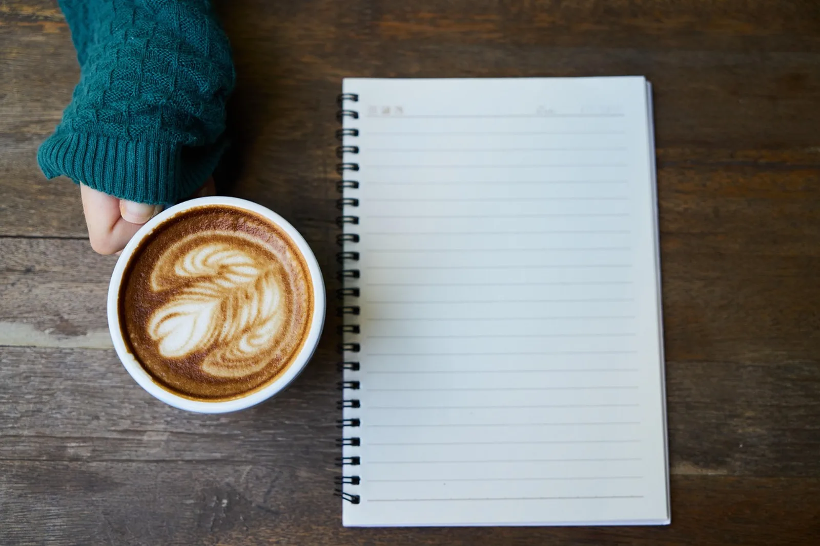 Woman who is nervous about her performance review sits calmly at an office desk with a coffee cup and a closed notebook