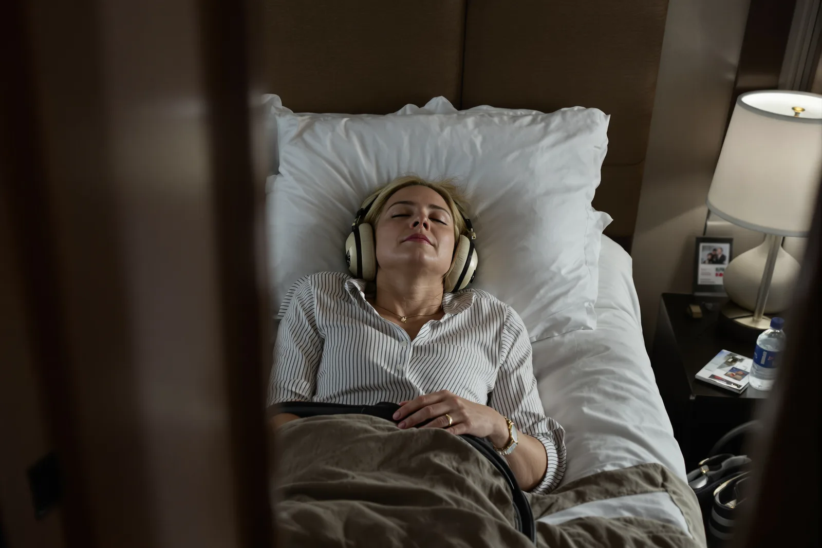 Woman lying in bed with eyes closed and headphones, listening to hypnosis audio while falling asleep