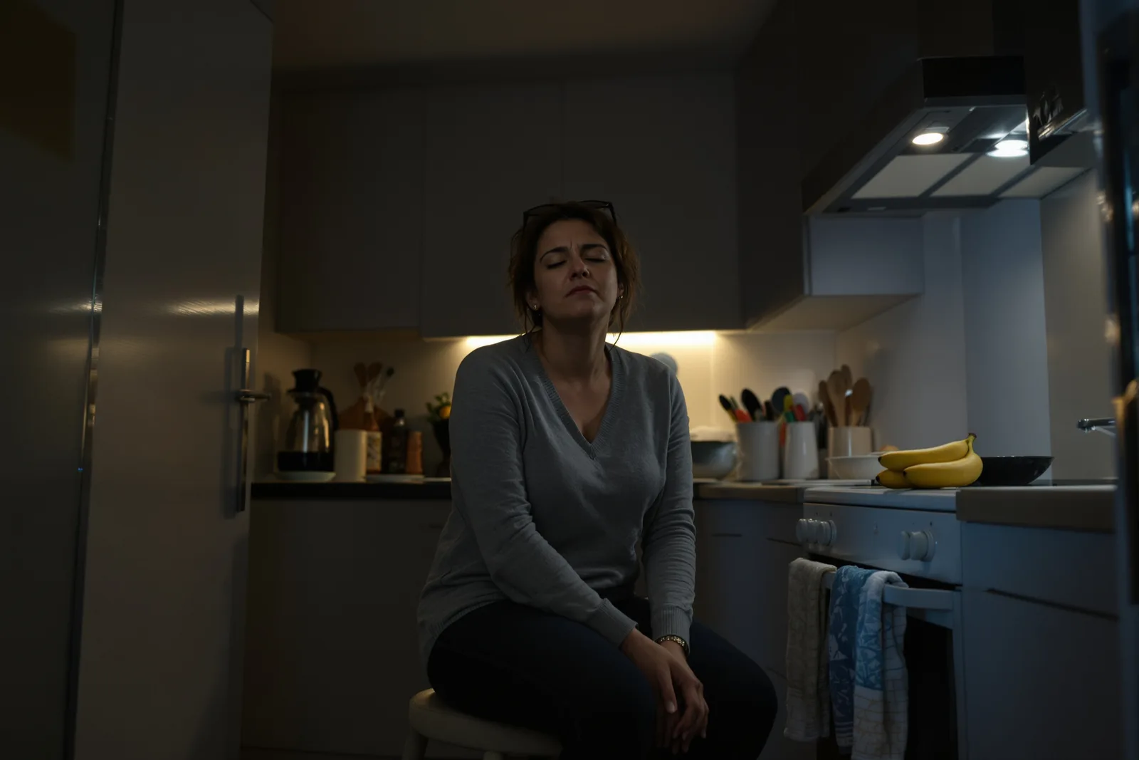 Woman sits tensely in her kitchen at night, eyes closed: a common reason self hypnosis is not working