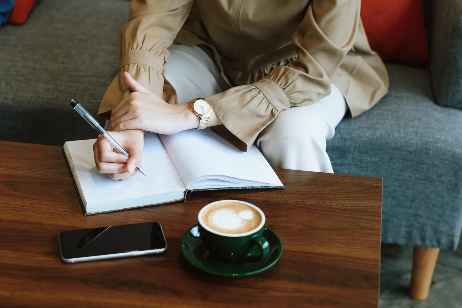 Woman writing a list in a notebook beside her coffee, the first step to prioritize tasks when everything is urgent