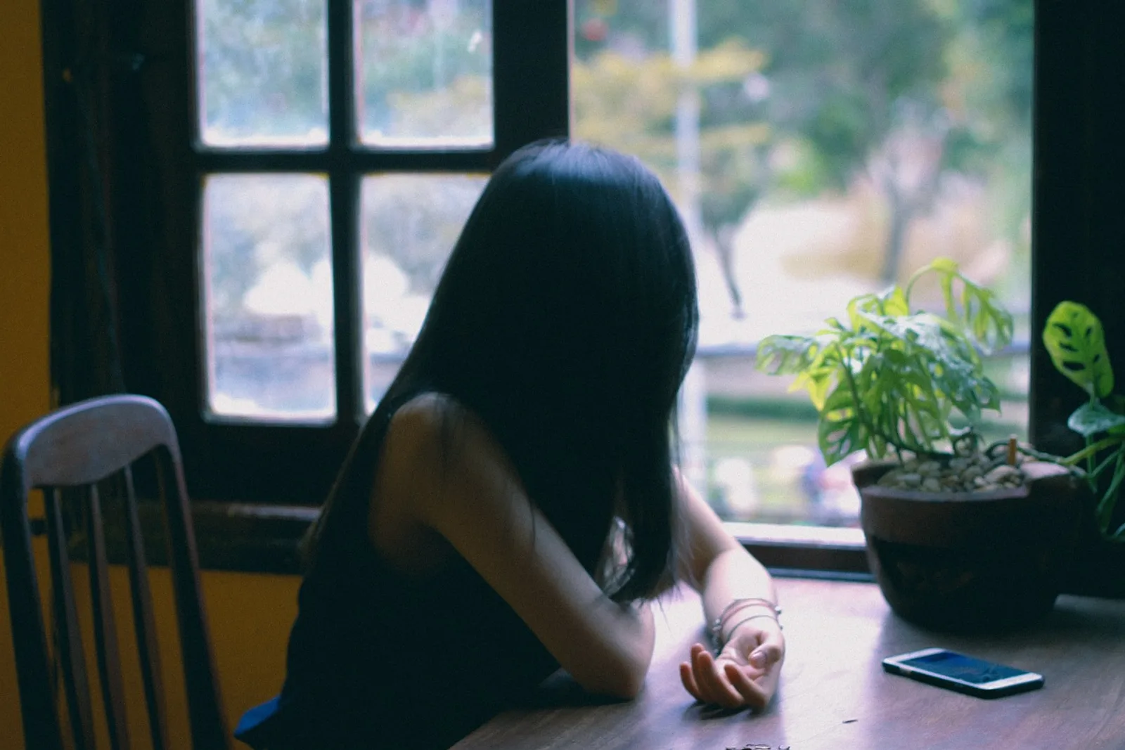 How to stop comparing your life to others: woman at the kitchen table puts her phone aside and looks out the window