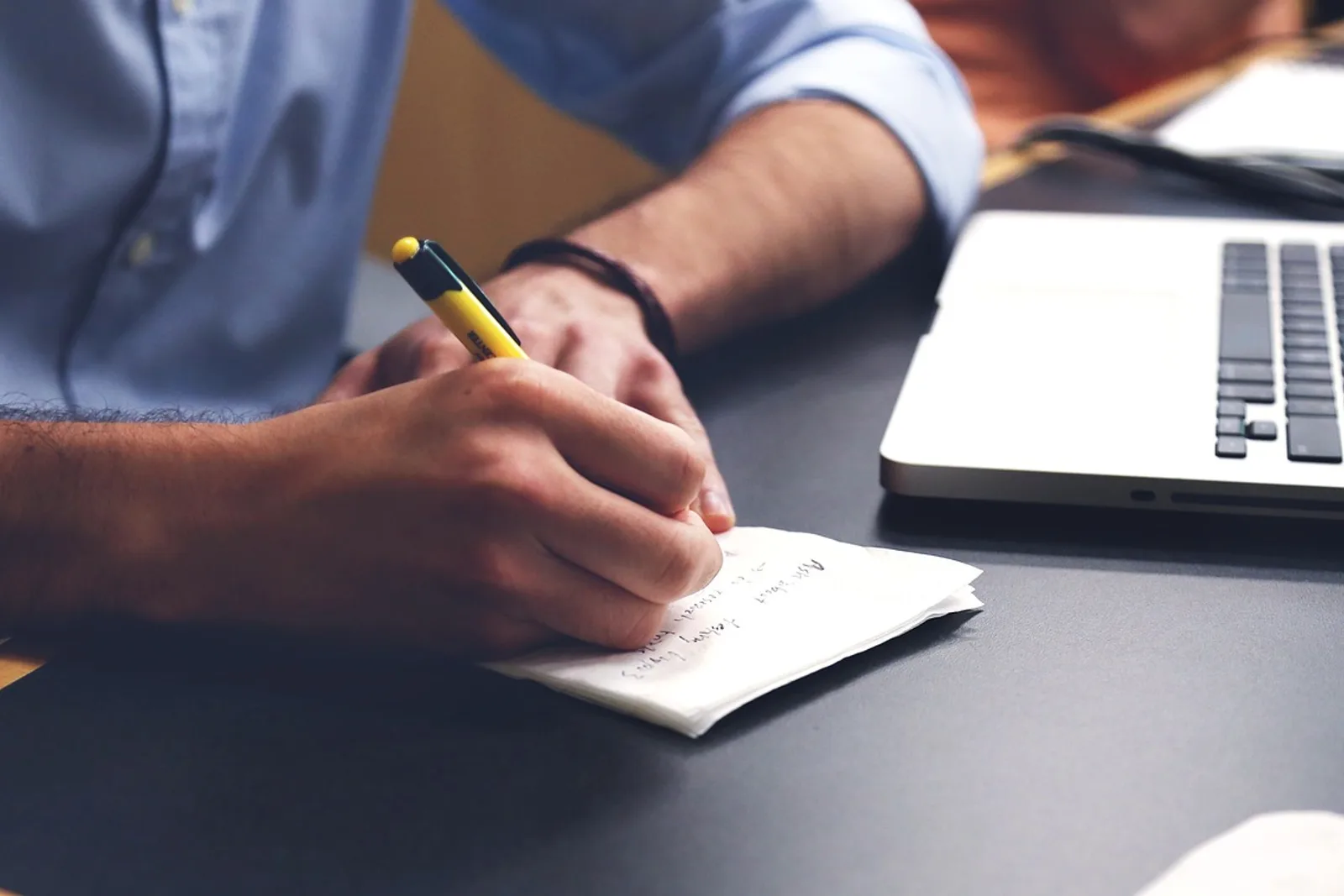 Man in a shirt jotting notes on paper next to his laptop to prepare for a salary negotiation