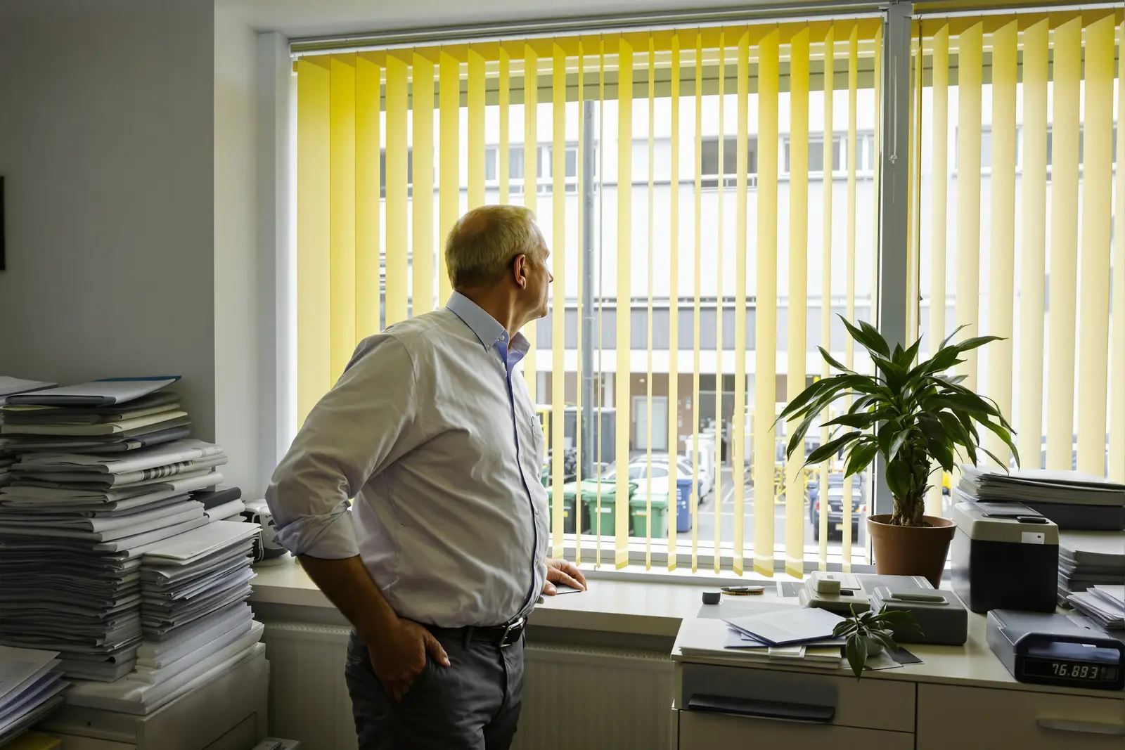 Mann steht im Büro zwischen Aktenstapeln und blickt aus dem Fenster: die Frage nach dem Sinn im Job