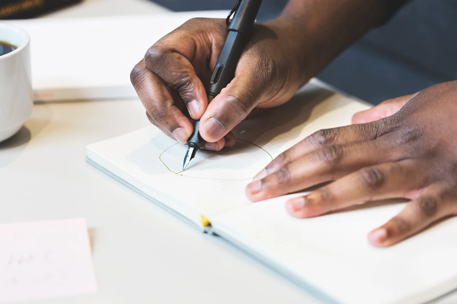 Hands drawing a circle in a notebook with a fountain pen: a writing exercise to find meaning in your work