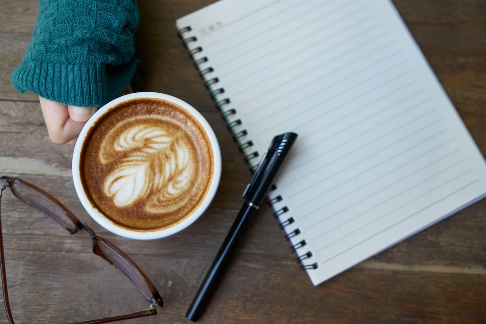 Frau mit Kaffeetasse an der Küchentheke legt die Hand auf ein offenes Notizbuch – Habit Stacking im Alltag