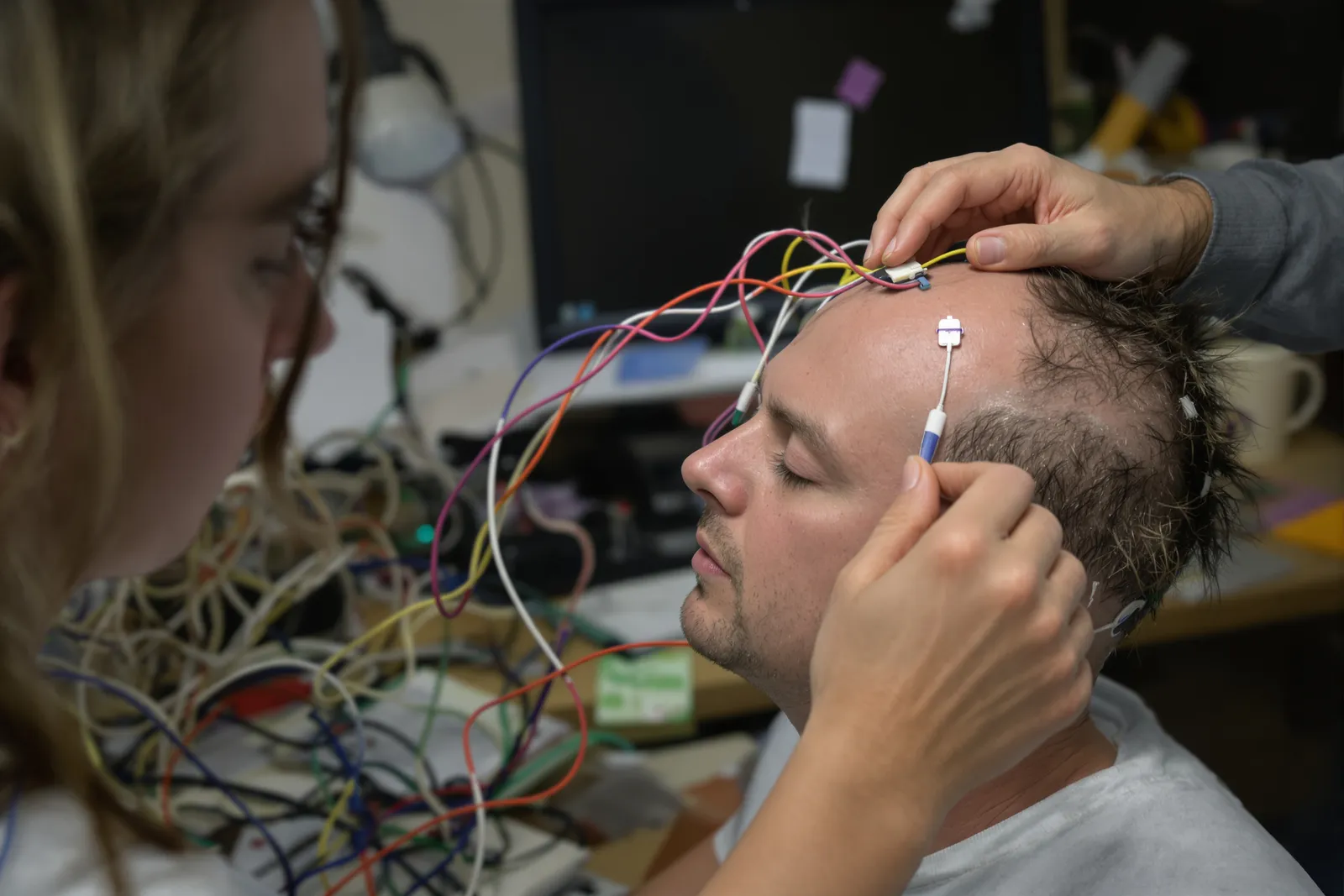 Researchers fitting EEG electrodes to a study participant with closed eyes: measuring how hypnosis works scientifically