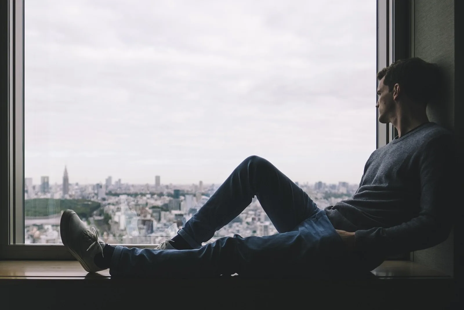 Man sitting relaxed on a windowsill looking out over the city, a calm inward moment far from the usual hypnosis myths