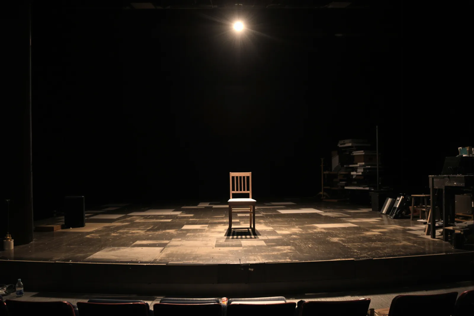 Empty wooden chair under a spotlight on a dark theater stage, symbolizing the stage hypnosis myth versus how hypnosis really works