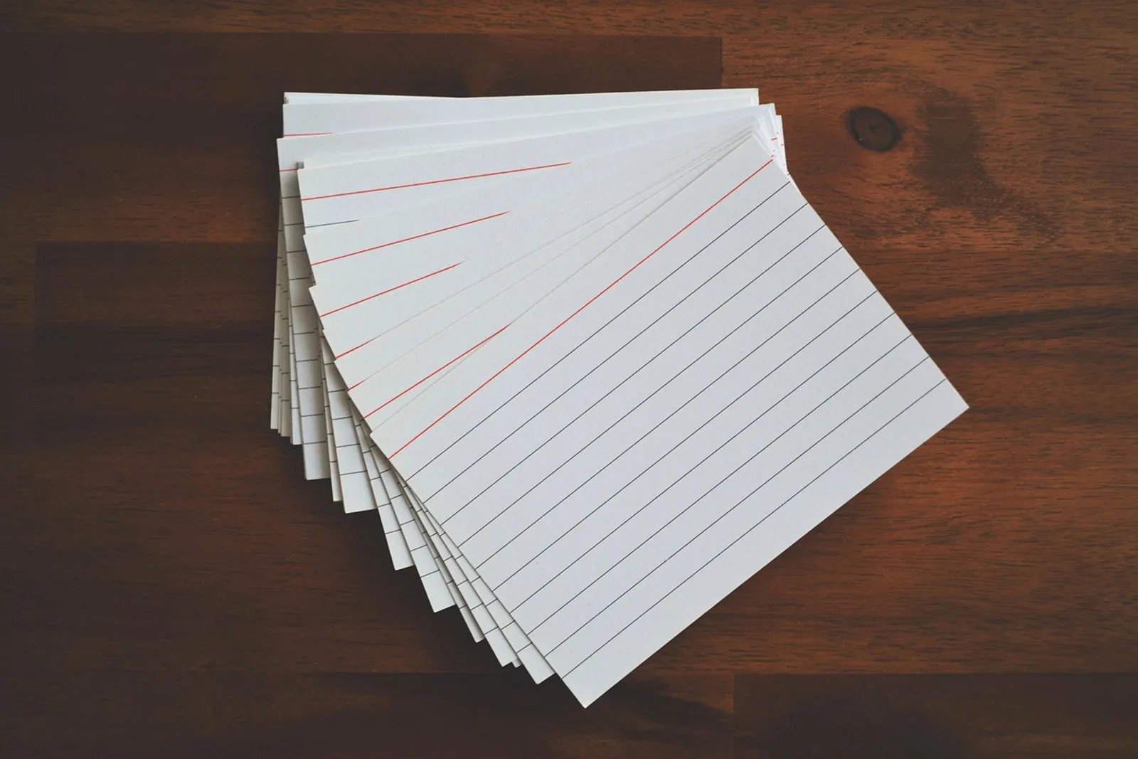 Stack of blank index cards fanned out on a wooden table: simple tools for backward planning to avoid deadline stress