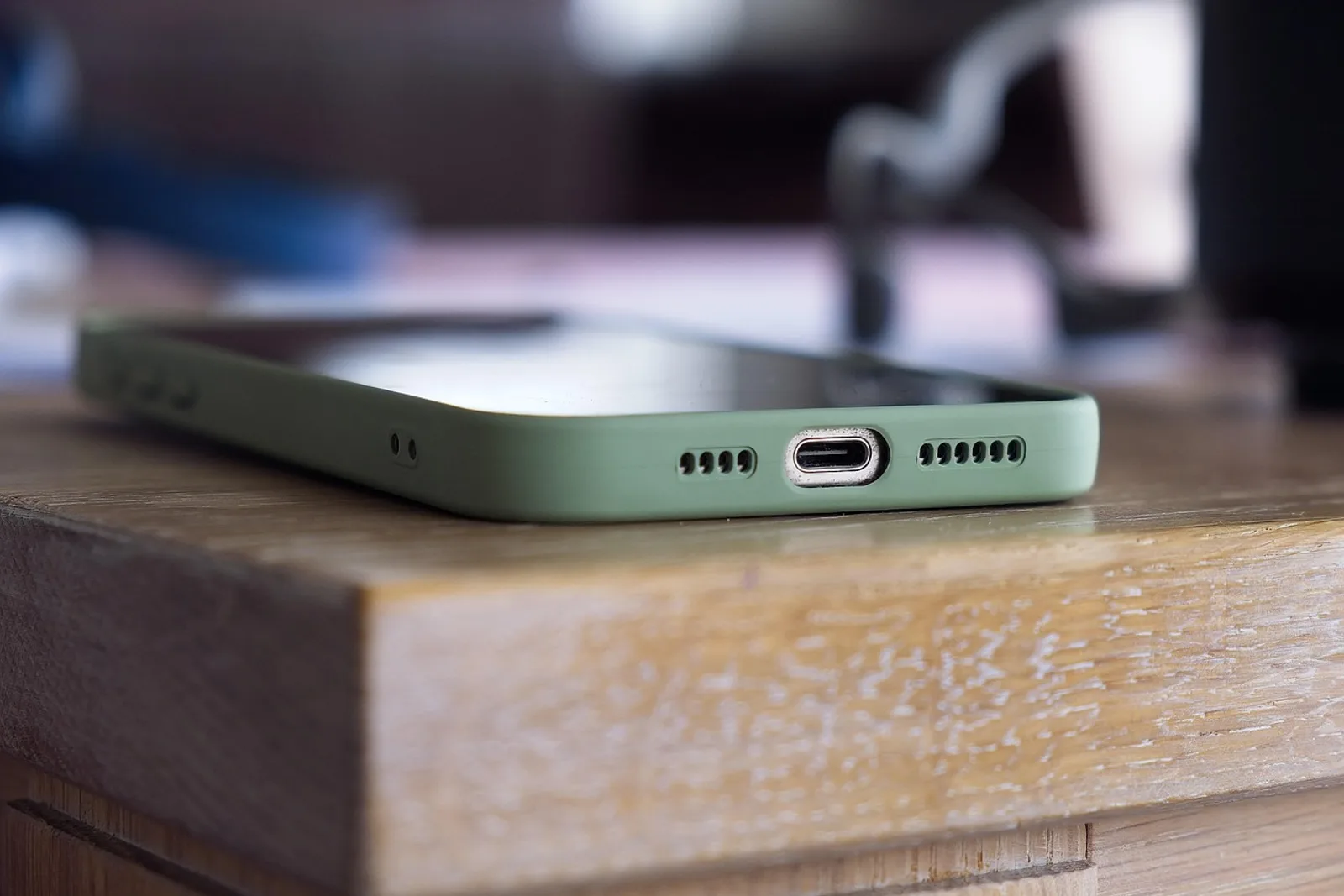 Smartphone in a green case lying face up at the edge of a wooden table, kept at a distance to avoid phone distractions