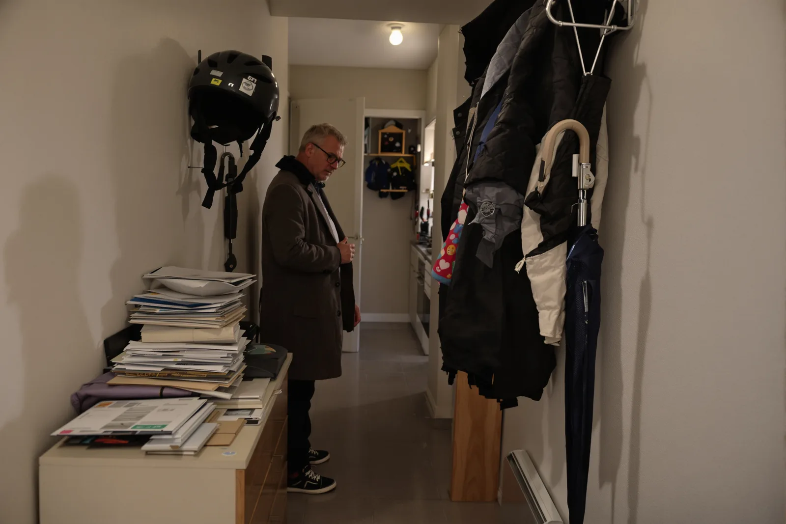 Mann im Mantel steht abends im Flur vor einem Stapel Post. Der innere Kritiker meldet sich oft beim Nachhausekommen