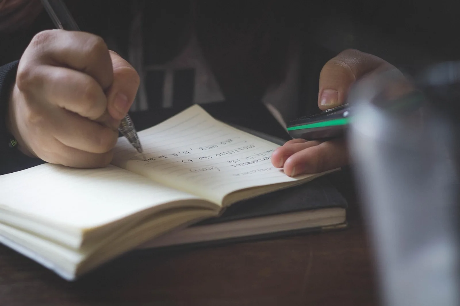 Hands writing in a notebook in soft evening light: an evening log to learn to accept compliments