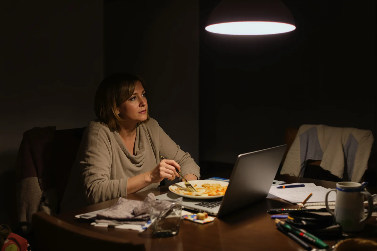 Frau isst abends allein am Tisch vor dem Laptop und starrt ins Leere: nicht abschalten können nach Feierabend