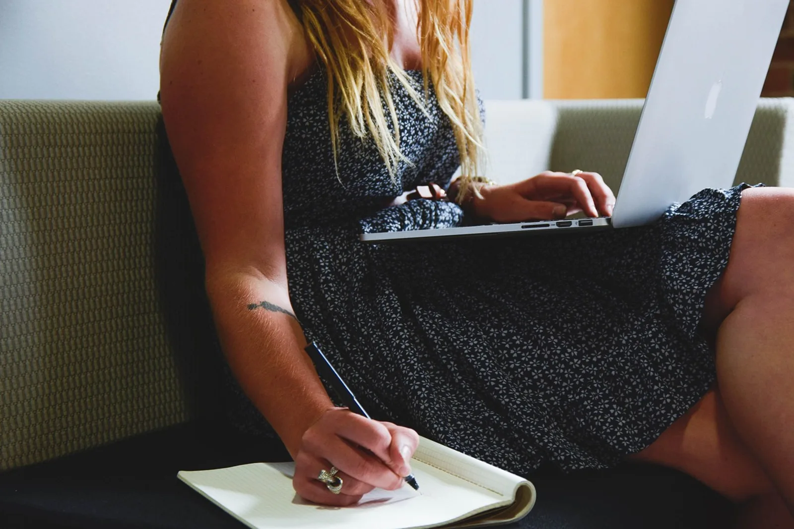 Woman with a laptop on the sofa writing thoughts in a notebook, a journaling exercise for self esteem